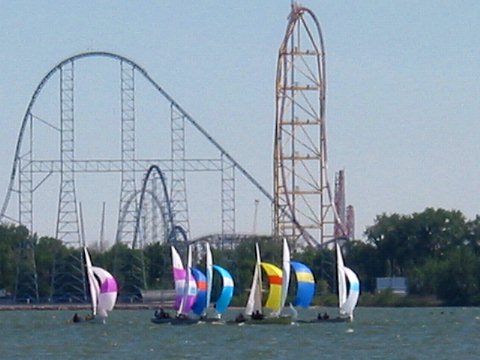 Seven sailboats flying spinnakers, framed by Cedar Point coasters